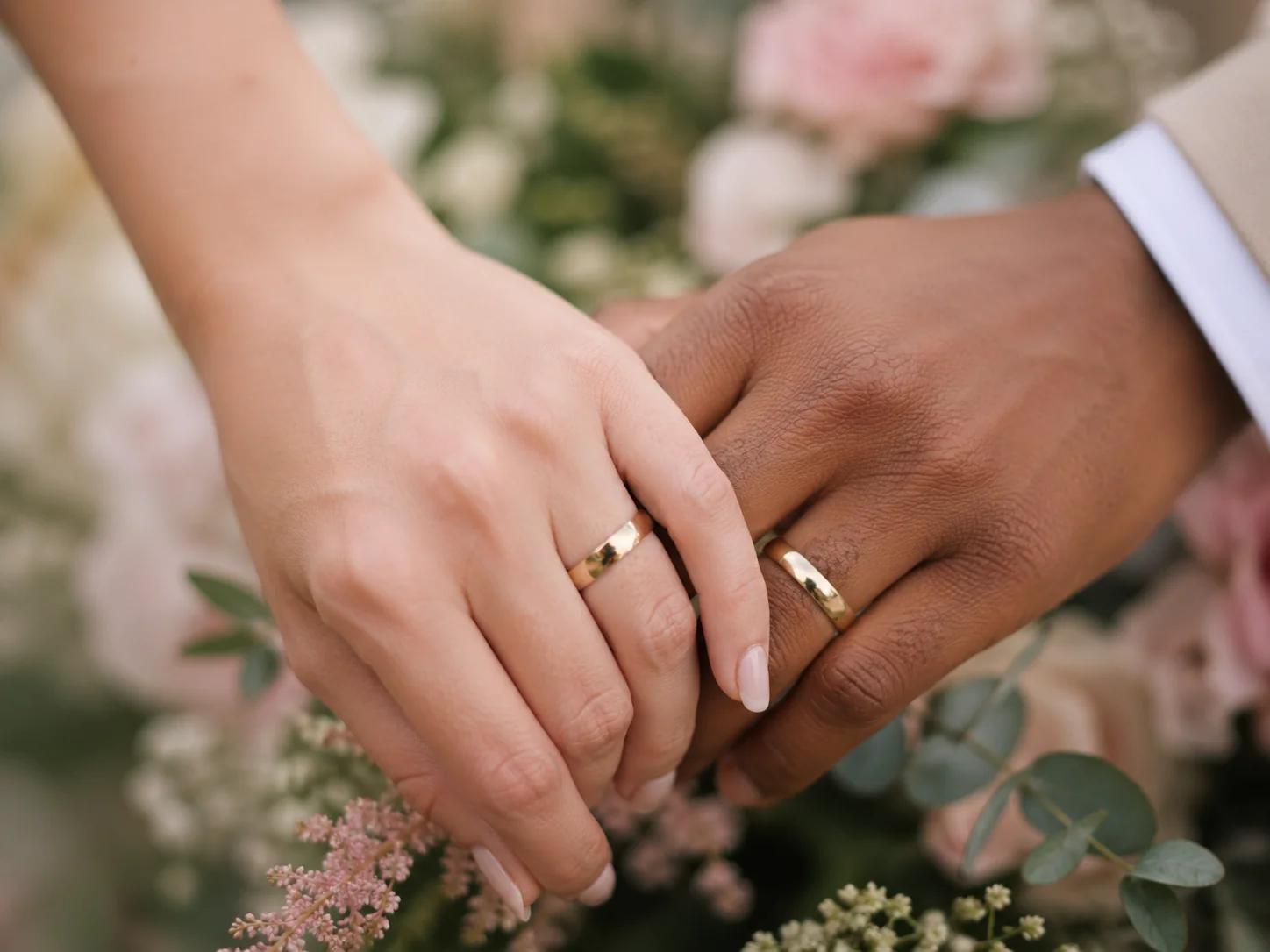 Mains entrelacées avec alliances dorées d'un couple mixte le jour de leur mariage